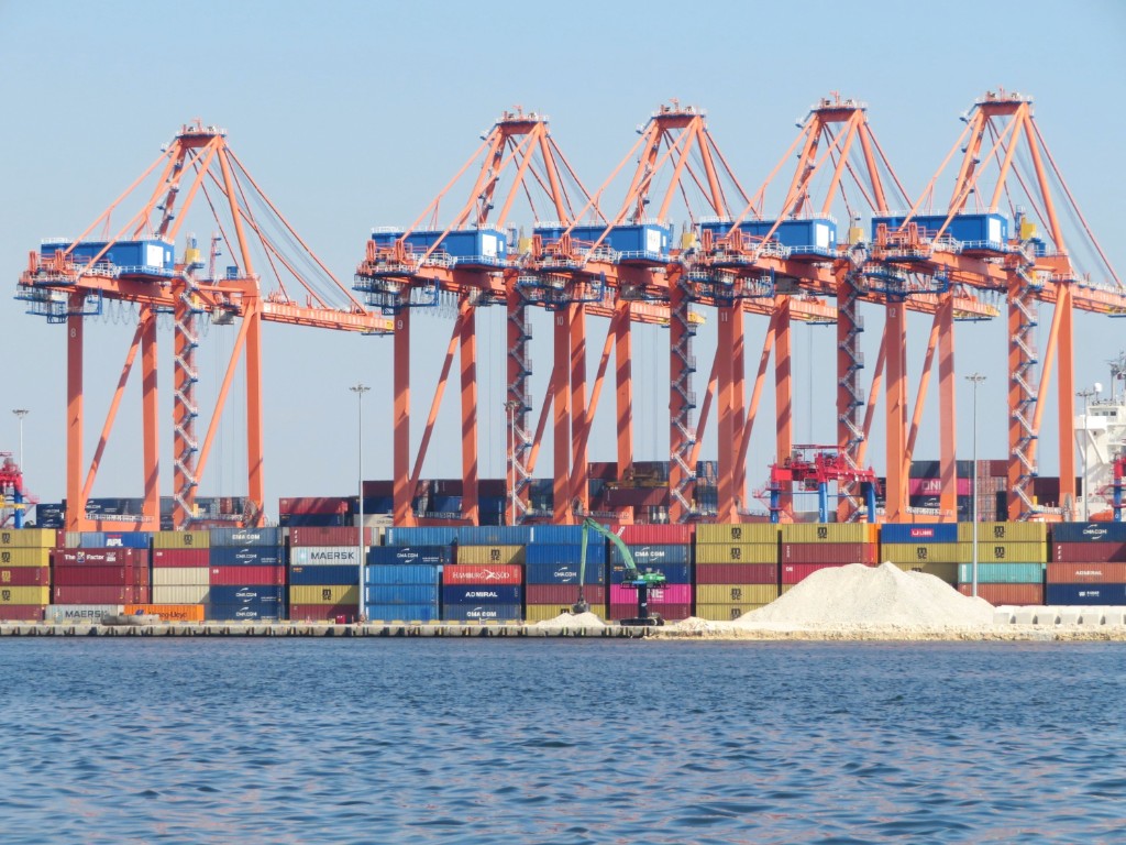 Orange gantry cranes and stacked colorful shipping containers at Mersin Port under a blue sky