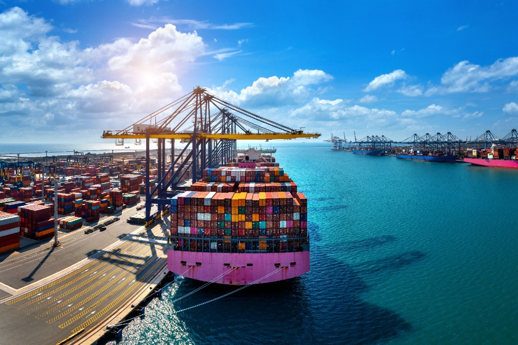 Container ship loaded at a busy harbor with yellow gantry cranes and stacked containers